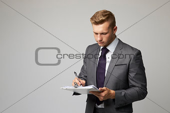Studio Portrait Of Businessman Writing On Clipboard