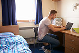 Male Student Working In Bedroom Of Campus Accommodation