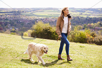 Mature Woman Taking Golden Retriever For Walk In Countryside