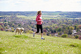 Mature Woman With Golden Retriever Jogging In Countryside