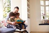 Father And Sons Reading Story At Home Together