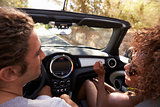 Happy young couple driving in open top car, woman clapping