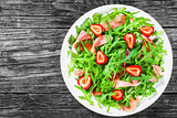 strawberry, arugula, prosciutto salad on the white dish on the old wooden rustic table, top view, closeup