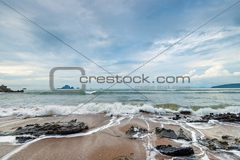 Sharp stones and sea foam on the sandy shore of Thailand