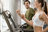 Determined young man smiling while running on treadmill during h