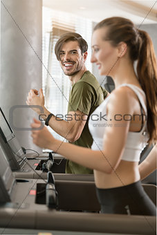 Determined young man smiling while running on treadmill during h