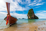 A wooden Thai boat with a motor on the background of a high clif