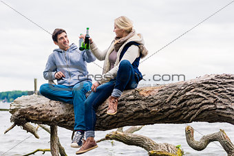 couple sitting on tree stump at the riverside drinking beer