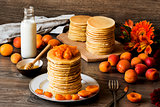 Stack of homemade american pancakes served with honey and apricots on wooden background