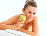 Portrait of smiling young woman showing apple while laying on ma