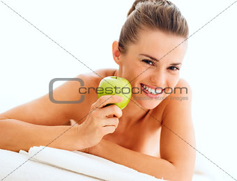 Portrait of smiling young woman showing apple while laying on ma