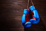 A pair of bright blue and red boxing gloves hangs against wooden background.
