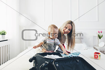 Travelling with kids. Happy mother with her child packing clothes for holiday