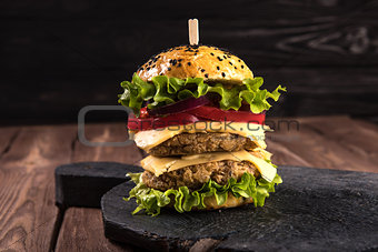 Homemade vegetarian double burger with two cutlets, tomato, cheese, green salad and purple onion on a dark wooden background