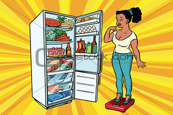 Diet. Young woman on scales, stand next to the refrigerator with