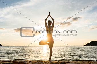 Silhouette of a woman practicing the tree yoga pose on a beach a