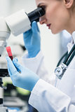 Woman examining blood sample under microscope in laboratory