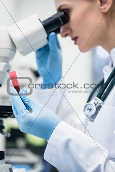 Woman examining blood sample under microscope in laboratory