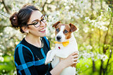 Happy young woman hugging and having fun with her Jack Russell Terrier In the blooming garden