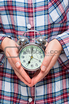 Close-up of an alarm clock in female hands on a background of pa
