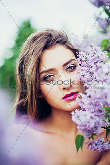 Portrait of young beautiful woman posing among lilac trees.