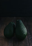 Two avocados on a dark, wooden background