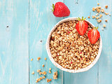 Top view of bowl with muesli and fresh strowberry on blue wooden background