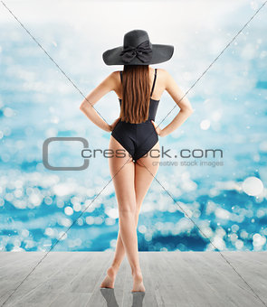 Woman in elegant black hat and swimsuit looks at sea