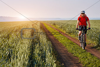 Young cyclist with mountain bicyclist on the path of the field in the countryside against sunrise.