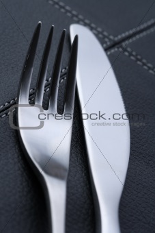 metal fork and knife with abstract blue light on black leather p