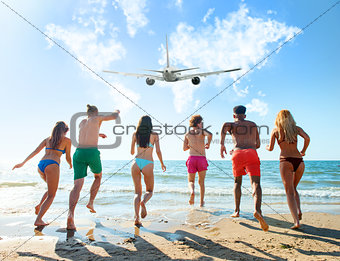 Group of friends run to the sea with an aircraft in the sky. Concept of travel and summer