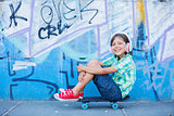 Cute boy with skateboard outdoors, standing on the street with different colorful graffiti on the walls