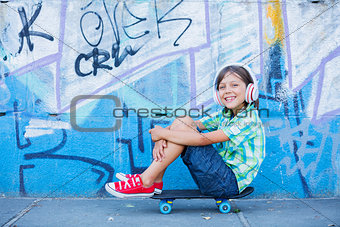 Cute boy with skateboard outdoors, standing on the street with different colorful graffiti on the walls