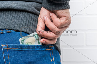 A man's hand pulls out dollars from the back pocket of jeans