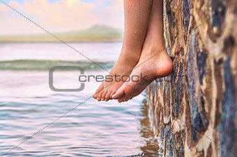 Young girl's feet dangling from the stone jetty