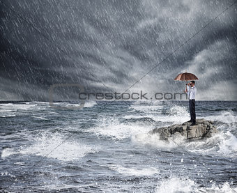Businessman with umbrella during storm in the sea. Concept of crisis