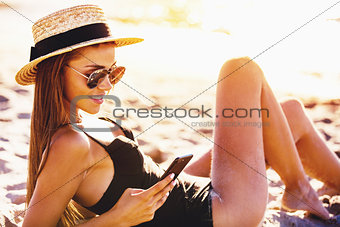 Beautiful girl sends a message with her smartphone at the beach