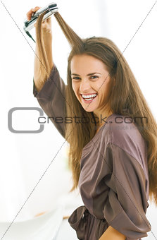 smiling young woman straightening hair with straightener