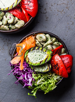 Budha bowl. Raw vegetables with beans, grilled avocado and bell pepper on slate background. Top view