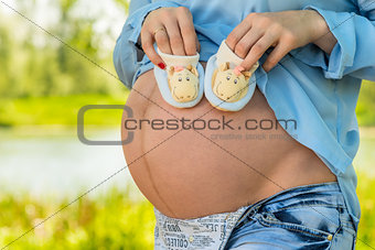 Belly of a pregnant woman close-up and booties in hands