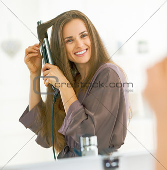 Smiling woman curling hair with straightener