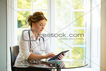 Young medical doctor woman seating at the table with sthetoscope and looking to the tablet