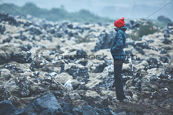 Woman hiker walks on volcanic Lava fields on background of mountains of Iceland.