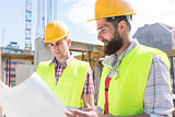 Two young construction workers analyzing together the plan of a