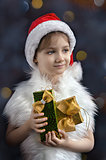 Little girl in hat of Santa Claus with gifts in his hands, colorful bokeh