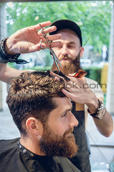 Dedicated hairstylist using scissors and comb while giving a coo