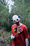 scary evil clown with a knife in the woods