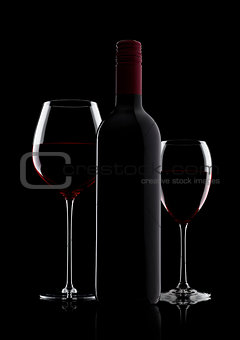 Glass of red wine with bottle with shape on black