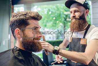 Dedicated hairstylist using scissors and comb while giving a coo