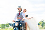 Bridal pair driving motor scooter wearing gown and suit